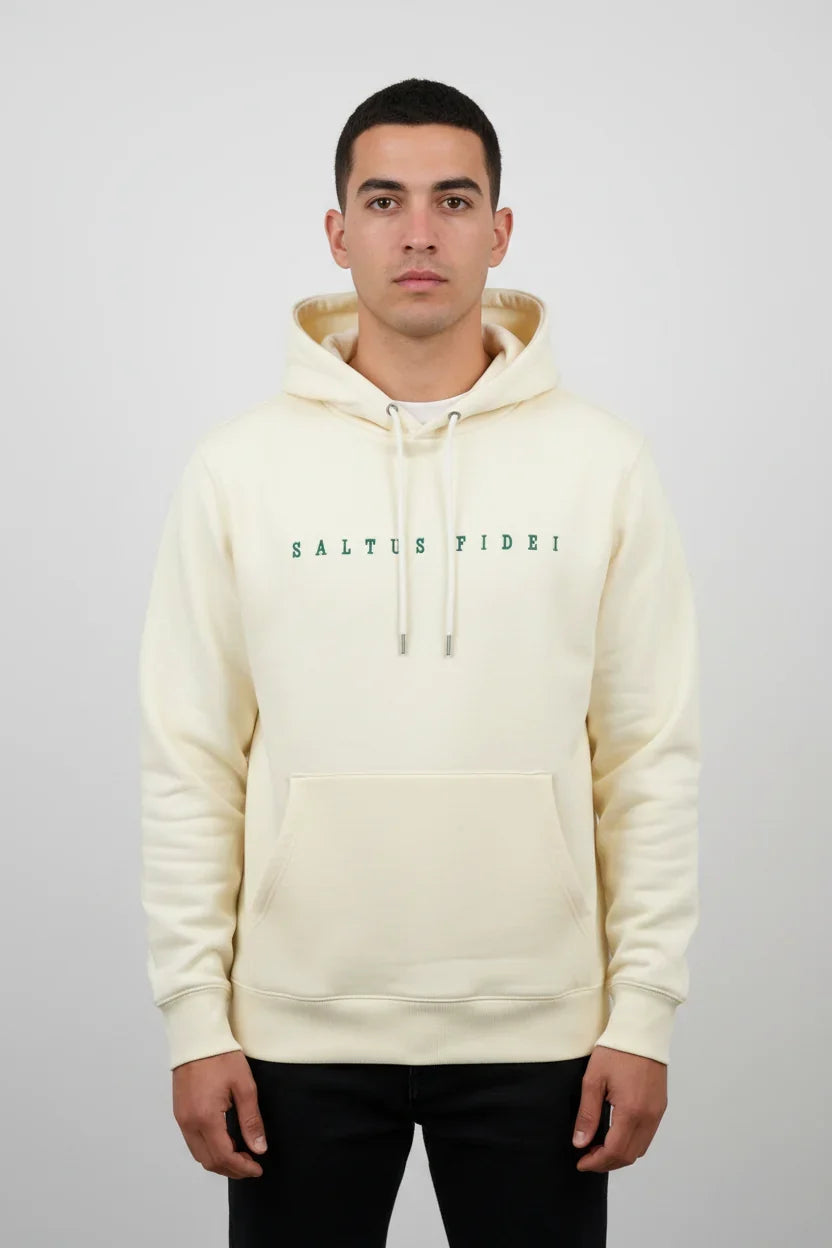 A man wearing an off-white Saltus Fidei heavyweight hoodie with green embroidered logo, black trousers, studio background