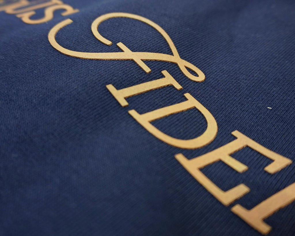 Close-up of a navy blue fabric surface with large brownish-beige silicone rubberised logo lettering partially visible, showing the word 'FIDE' in an elegant script and serif font.