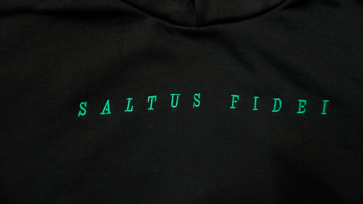 Close-up of a black hoodie featuring the phrase 'SALTUS FIDEI' printed across the chest in a bright green serif font.